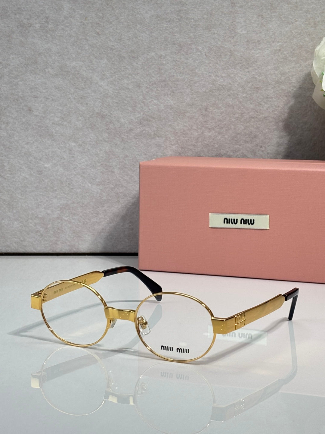 Round eyeglass frames with clear lenses, gold-toned arms, Miu Miu logo.