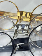 Close view of eyeglass frames with clear lenses, gold and silver metal, Miu Miu logos.