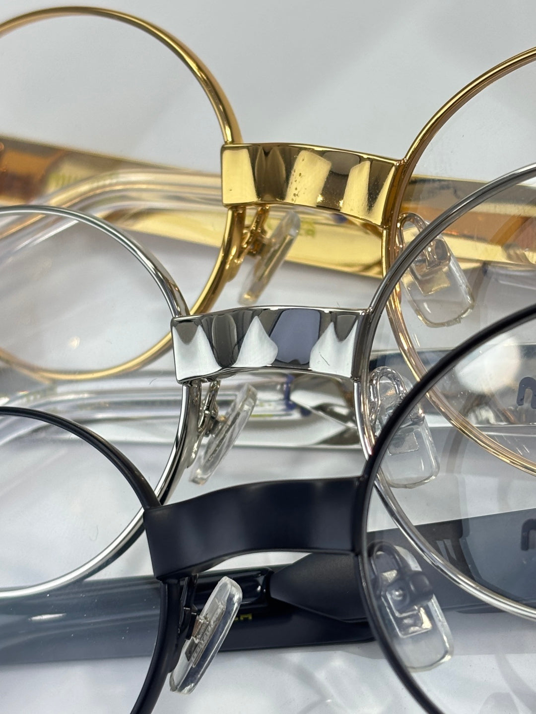 Close view of eyeglass frames with clear lenses, gold and silver metal, Miu Miu logos.