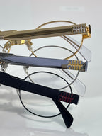 Close view of multiple eyeglass frames: gold arms and dark blue temples, Miu Miu logos.