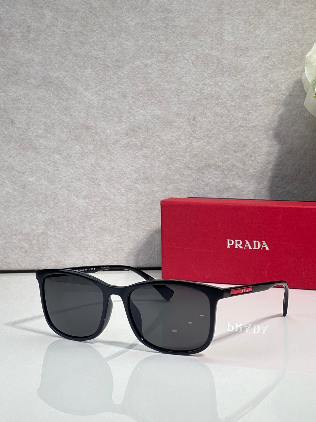 Prada sunglasses with dark lenses and black tortoiseshell frames, next to red logo case