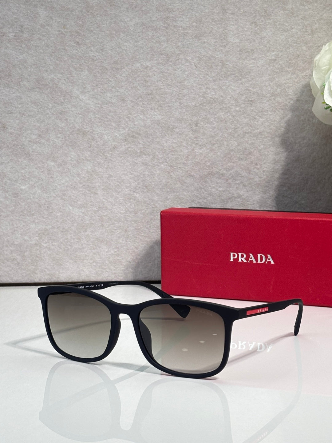 Prada sunglasses with brown-tinted lenses and black tortoiseshell frames, with red case behind