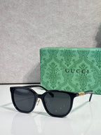 Black square sunglasses with dark lenses and gold Gucci logo on temples