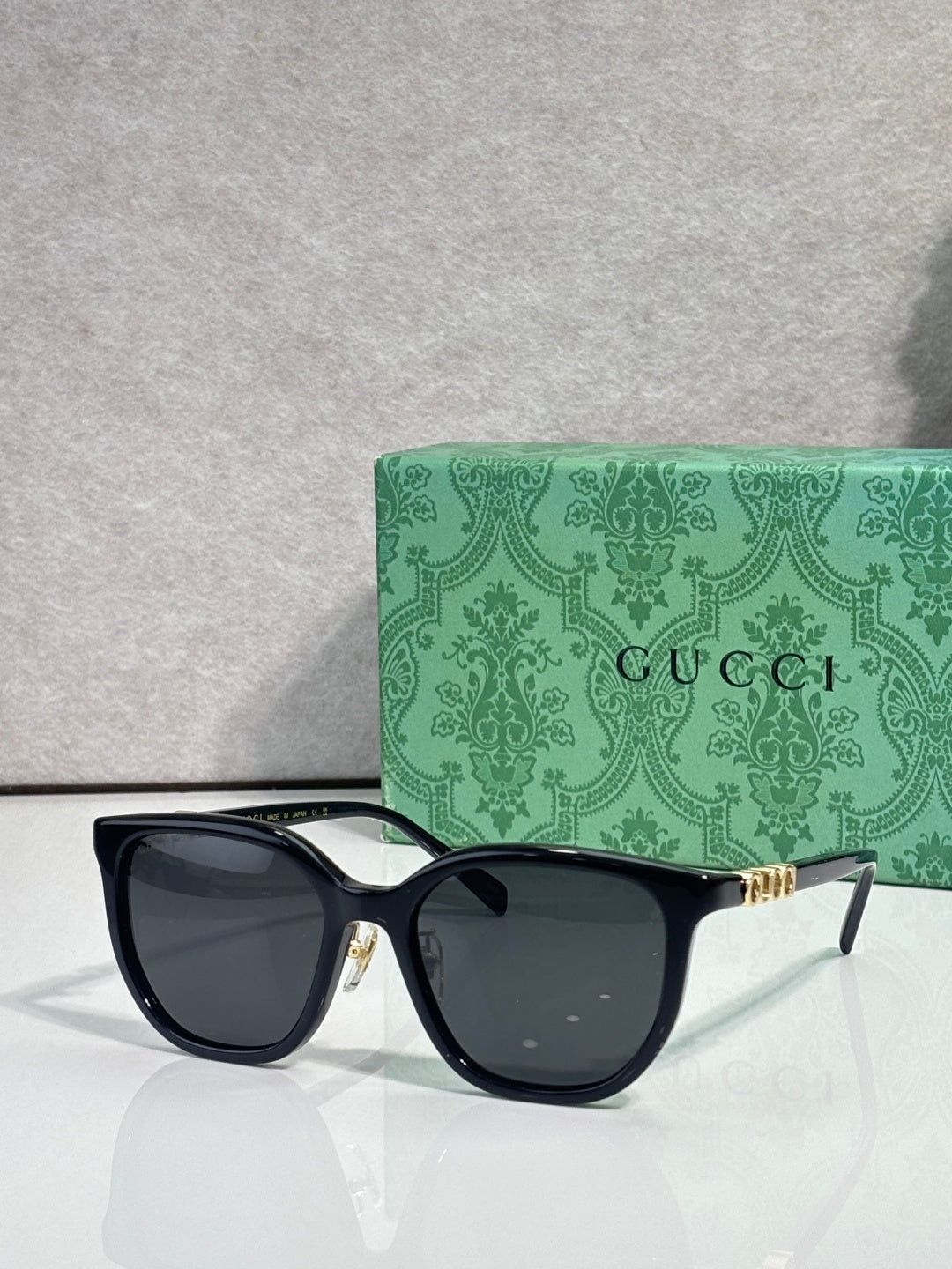 Black square sunglasses with dark lenses and gold Gucci logo on temples