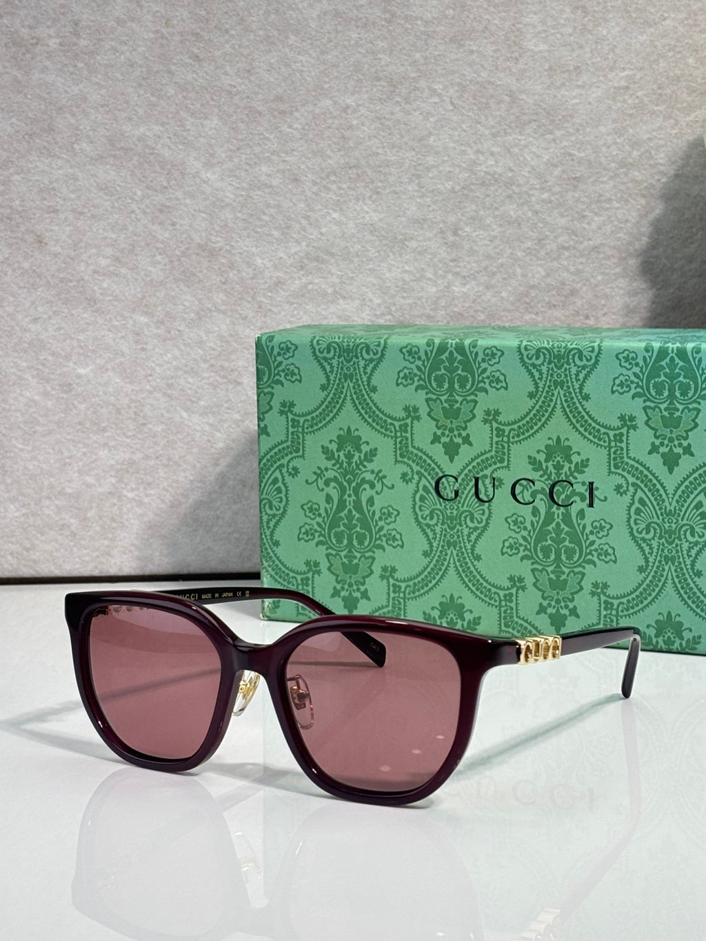 Burgundy square sunglasses with pink-tinted lenses and gold Gucci logo on temples