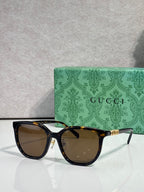Black square sunglasses with brown lenses and gold Gucci logo on temples