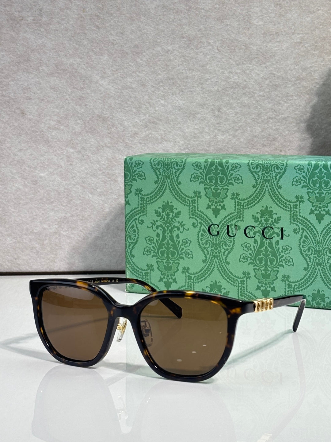 Black square sunglasses with brown lenses and gold Gucci logo on temples