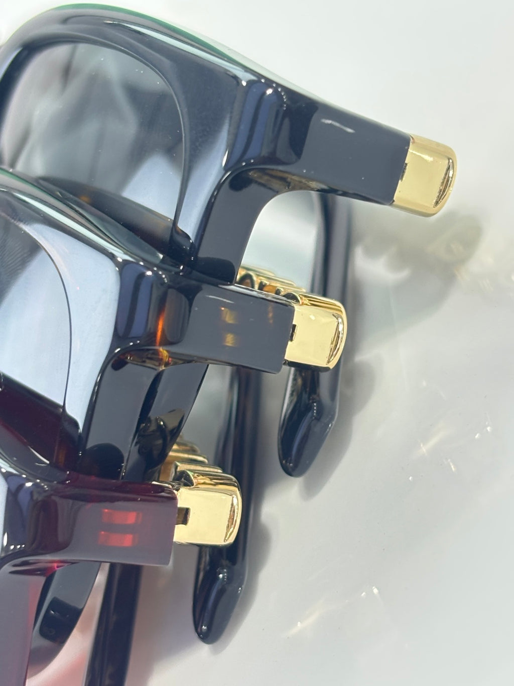 Glossy black sunglasses with gold hinge accents and tinted lenses