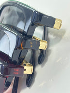 Glossy black sunglasses with gold hinge accents and tinted lenses
