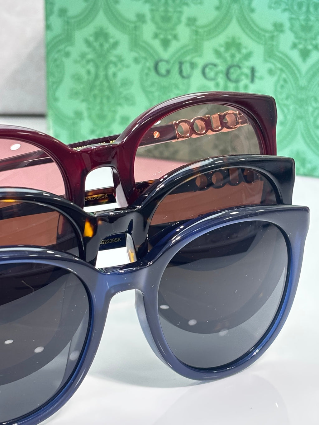Layered view of Gucci sunglasses: maroon and dark blue frames with tinted lenses