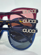 Gucci sunglasses close-up: maroon and dark blue frames with gold “GUCCI” logos