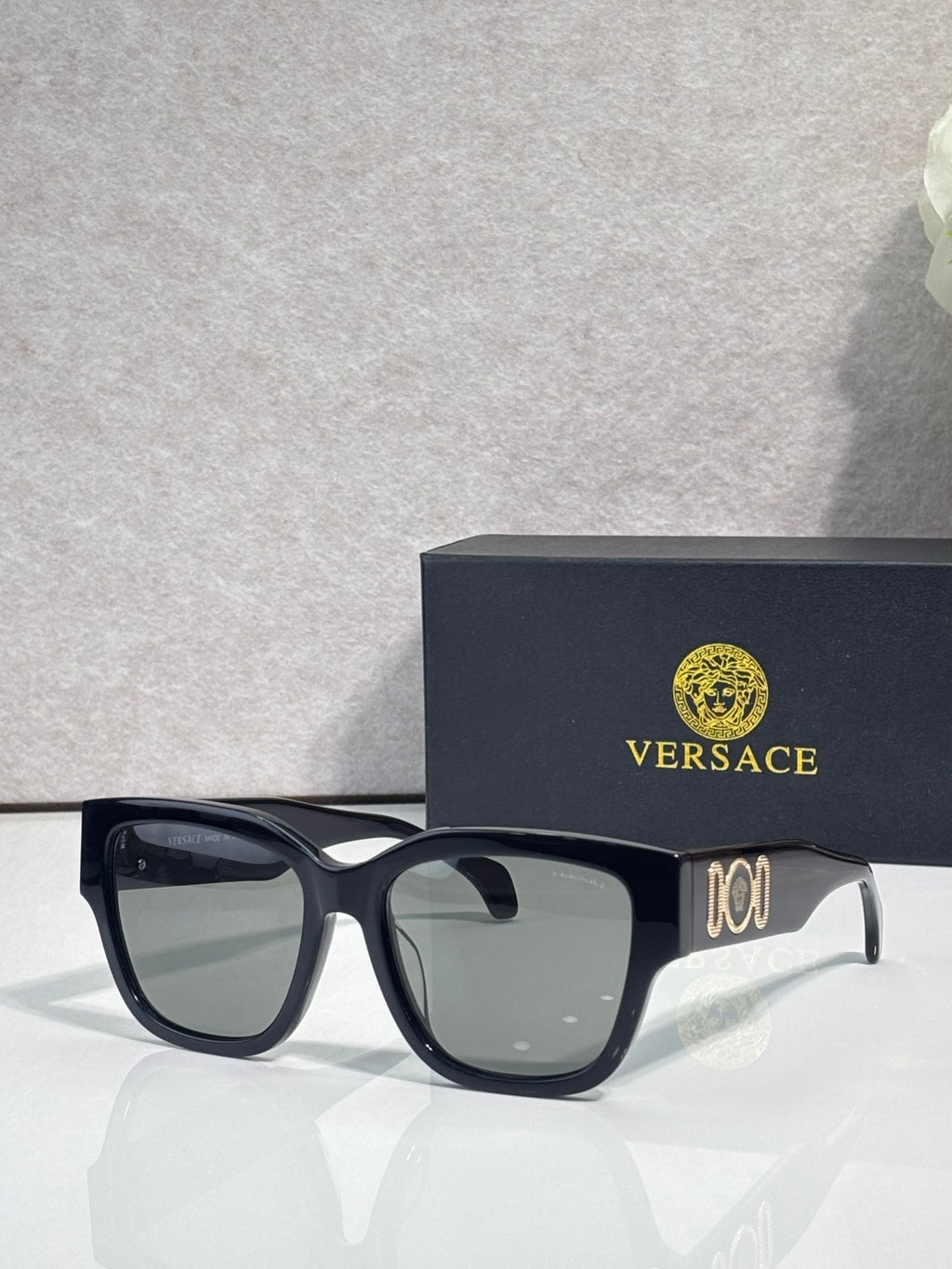 Versace sunglasses with black acetate frame and clear-tinted temples, gold logo detail.