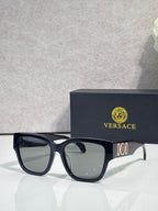 Versace sunglasses with black acetate frame and clear-tinted temples, gold logo detail.