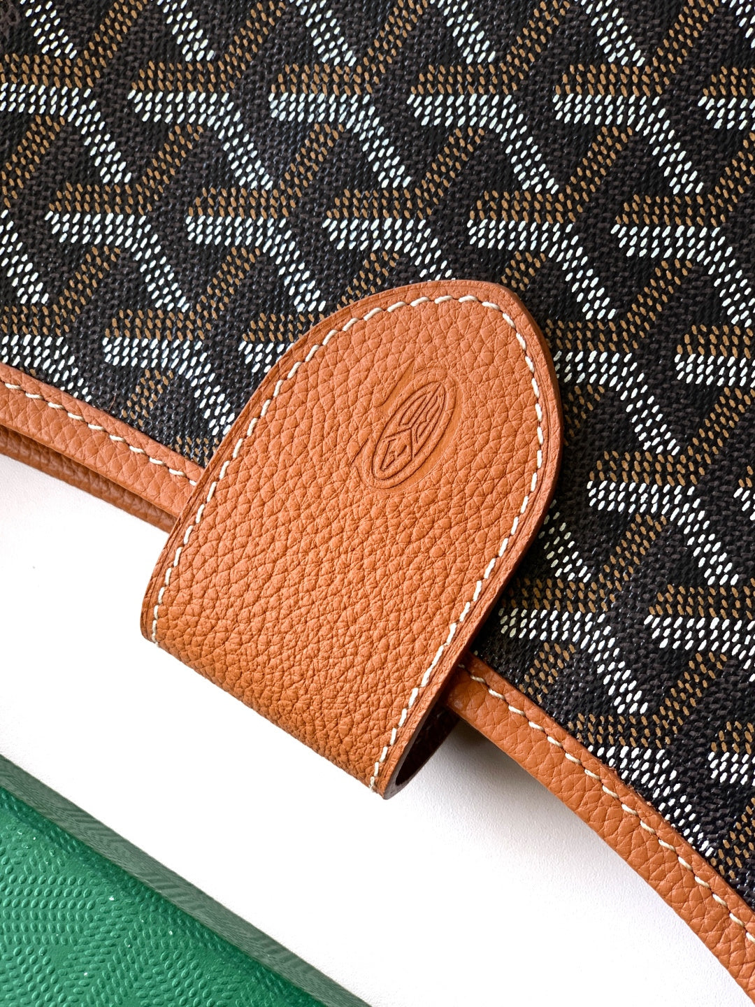 Tan leather mini pouch with stitched edge and embossed circular logo, close-up