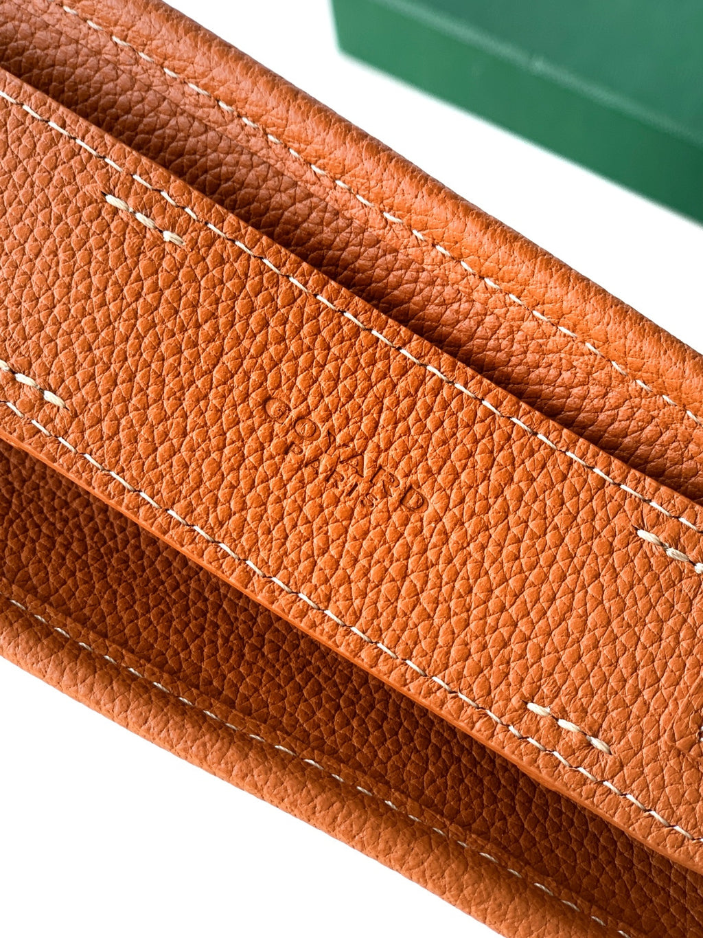Tan leather base with contrast stitching along edge, close-up