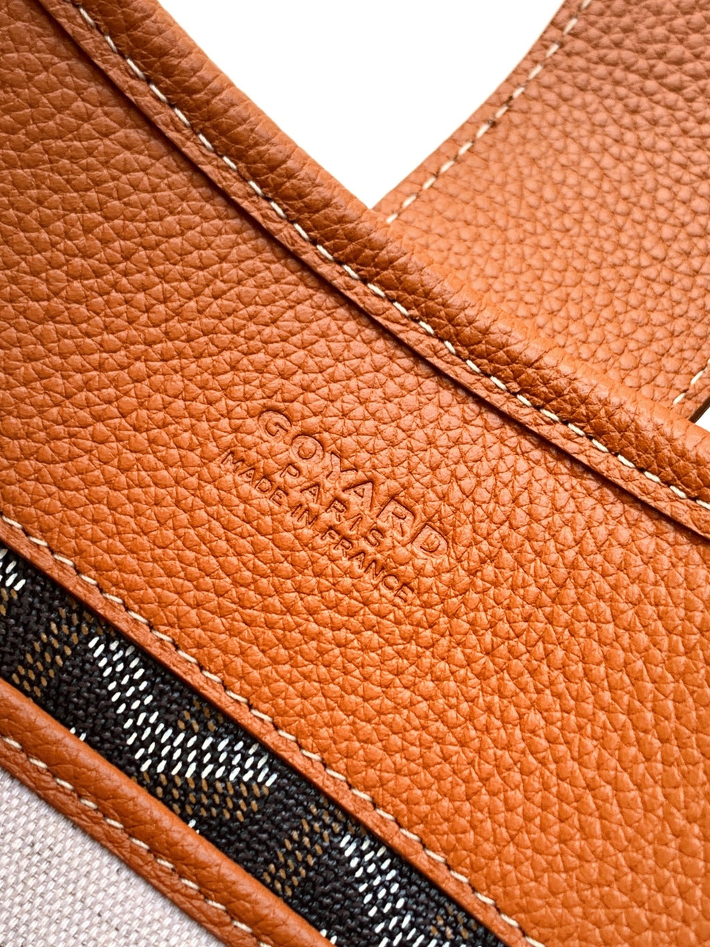 Tan leather side panel with embossed logo and stitched seam, close-up