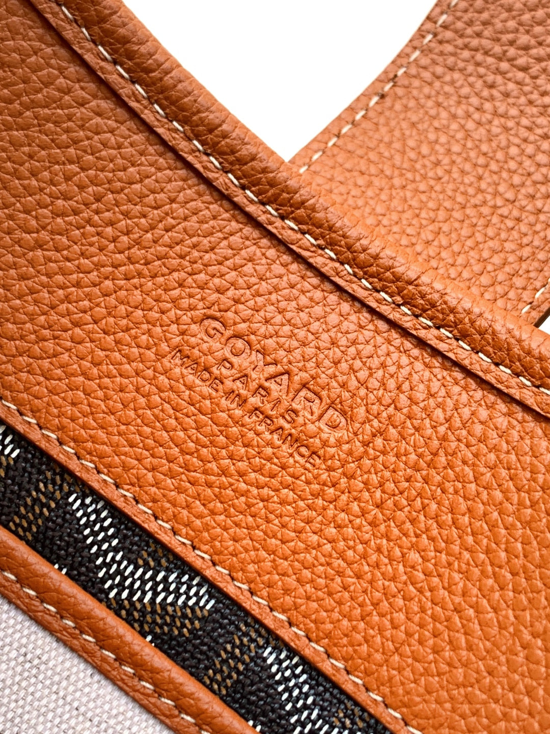 Tan leather side panel with embossed logo and stitched seam, close-up