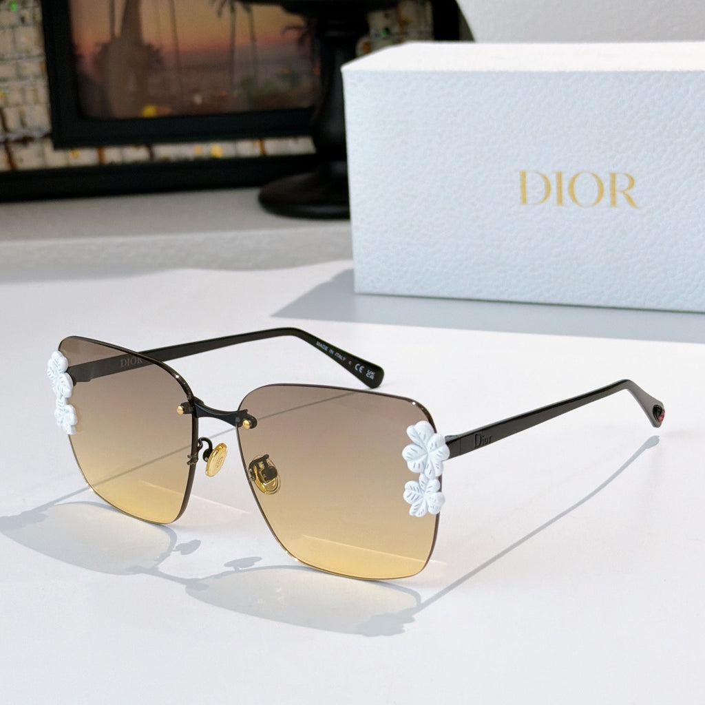 Dior sunglasses with black frame and amber gradient lenses, white floral temple accents.