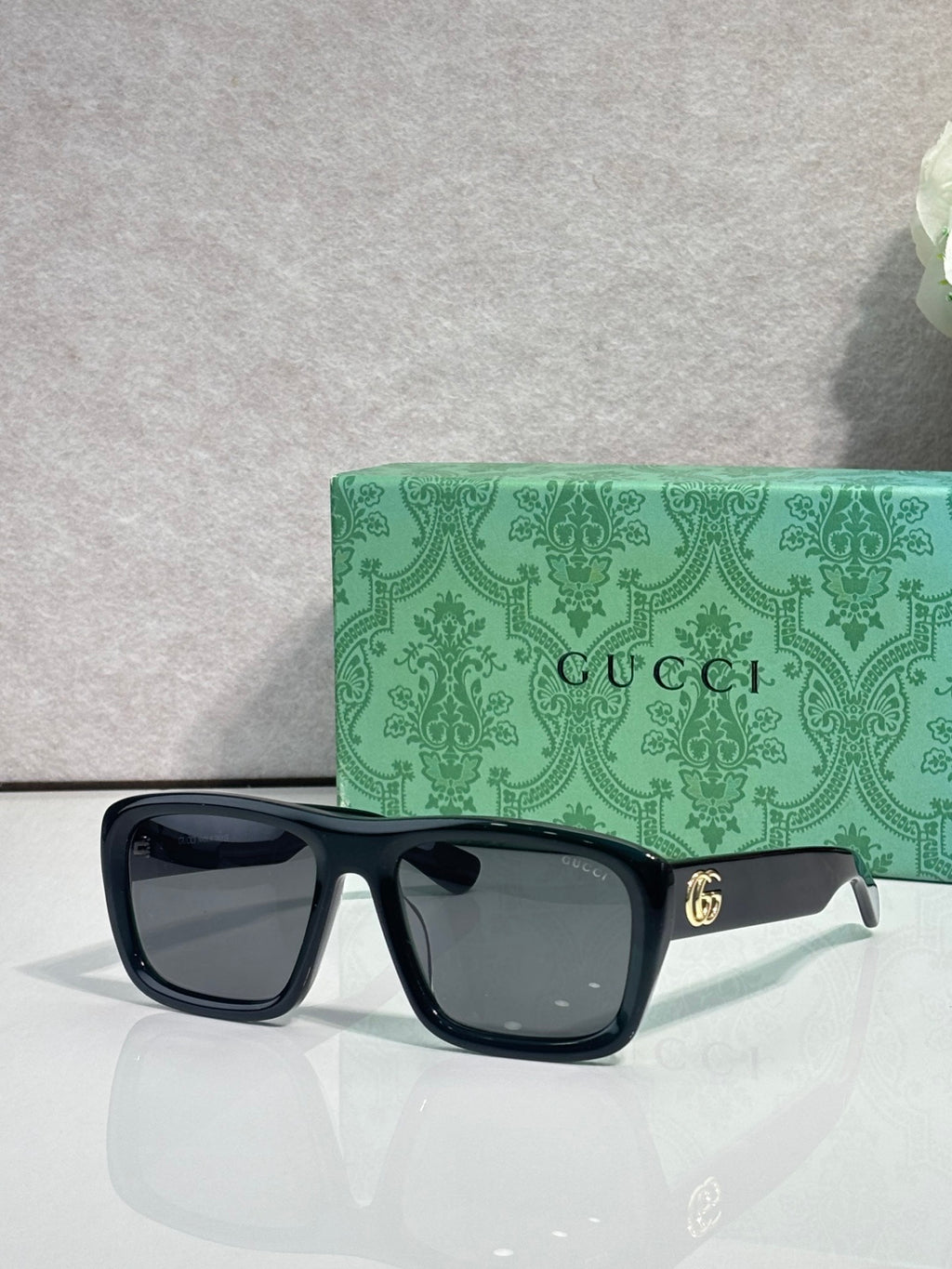 Gucci rectangular sunglasses with dark frames and clear lenses; gold GG detail on arm
