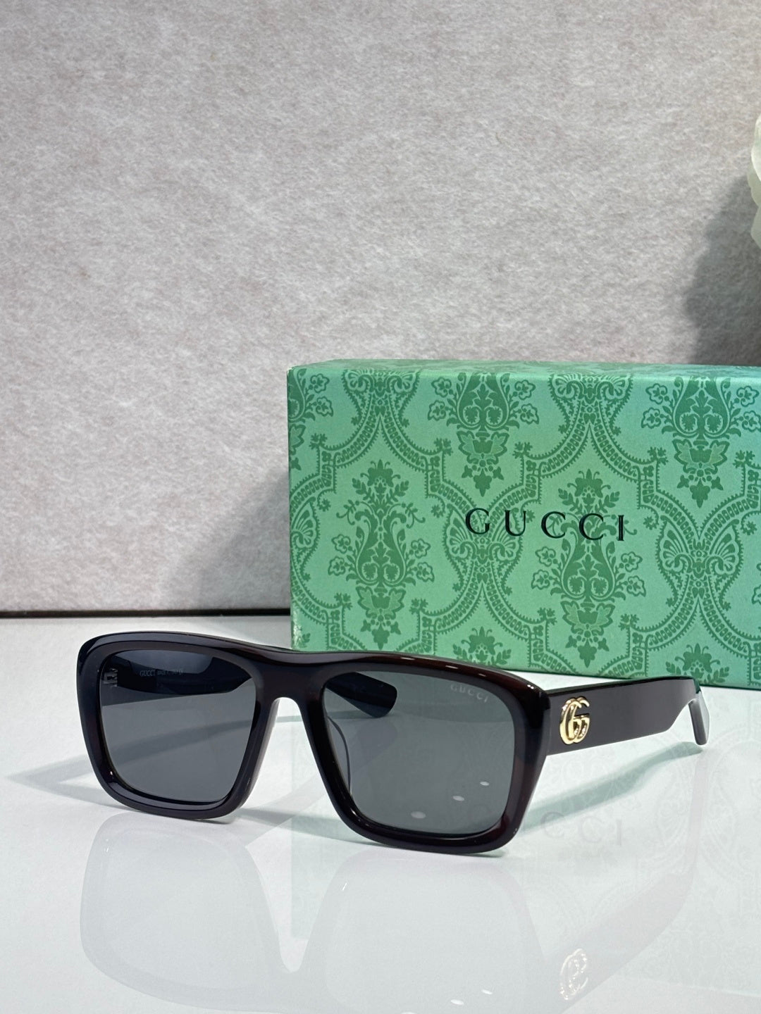 Gucci rectangular sunglasses with dark frames and dark lenses; gold GG temple logo