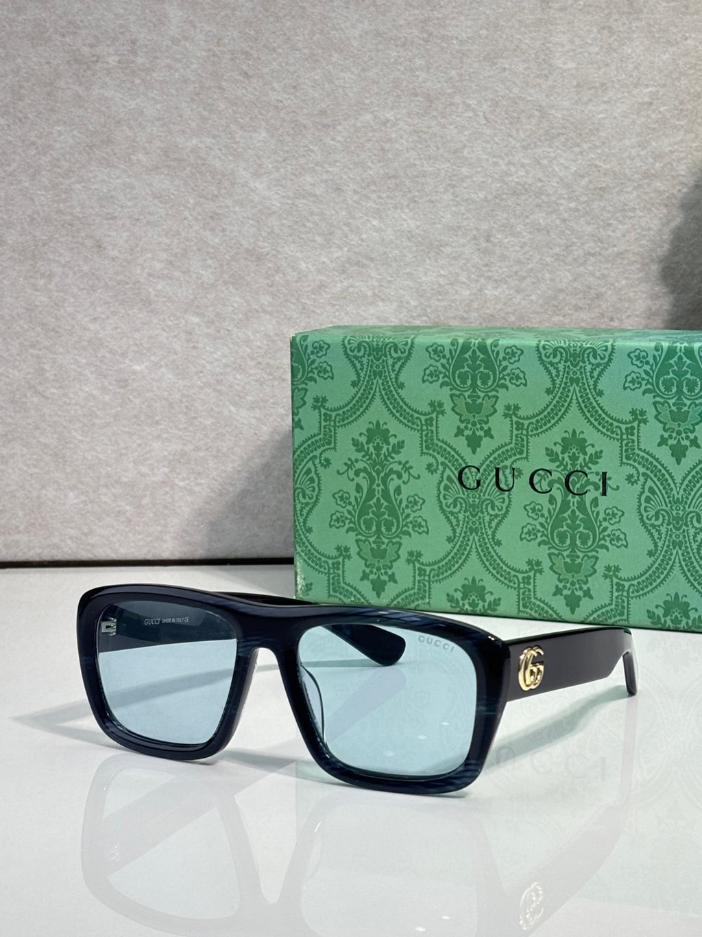 Gucci rectangular sunglasses with dark frames and light blue-tinted lenses; gold GG temple