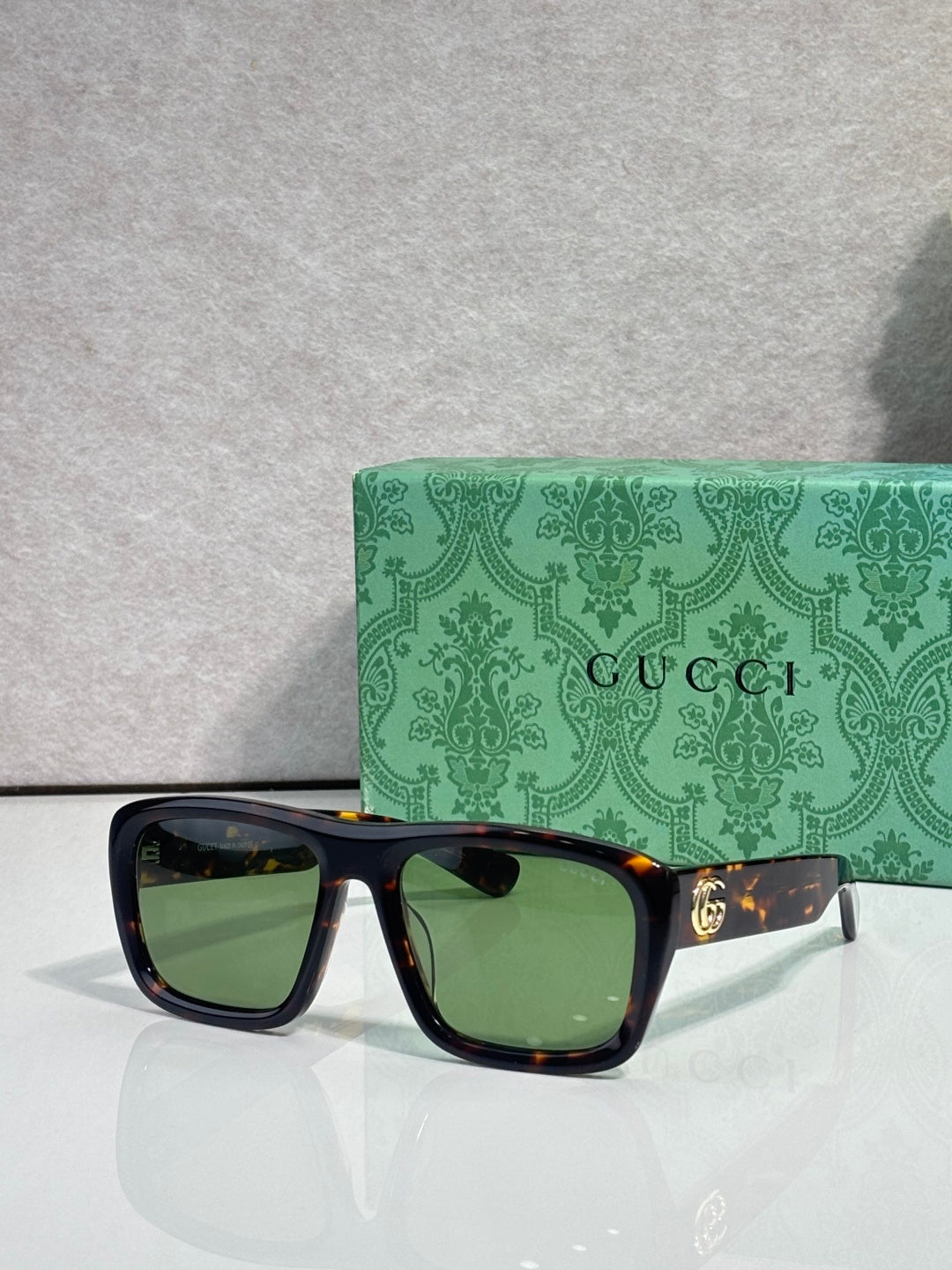 Gucci rectangular sunglasses with dark frames and green-tinted lenses; gold GG temple logo