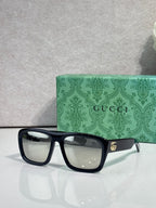 Gucci rectangular sunglasses with dark frames and clear lenses; gold GG logo on temple