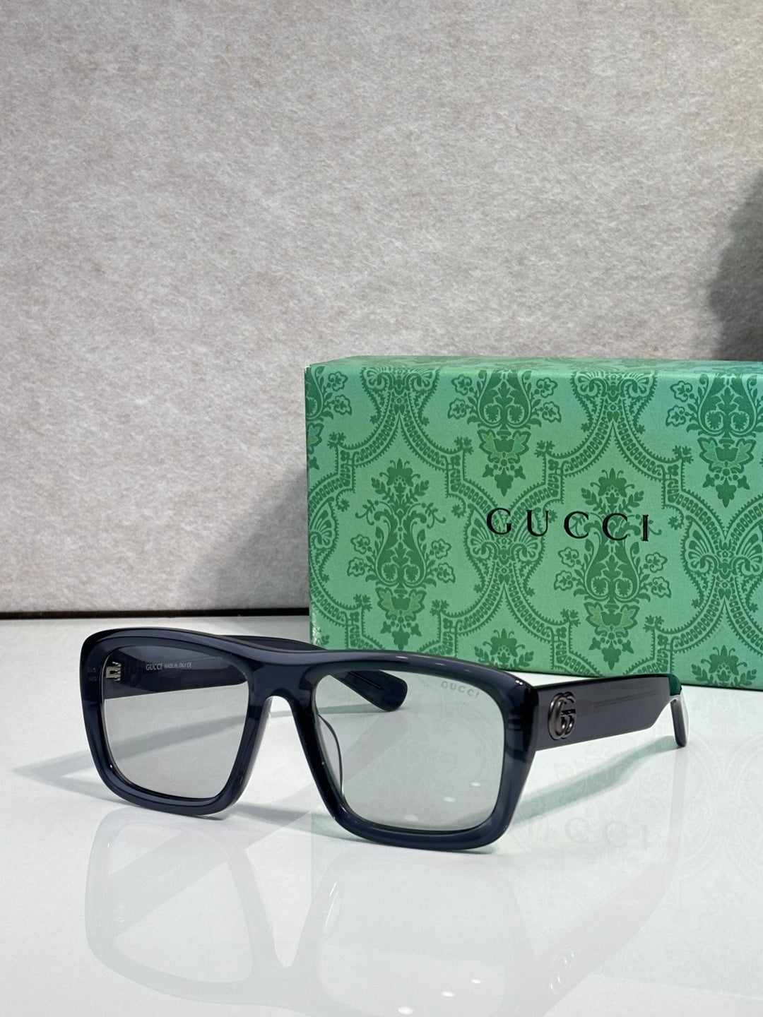 Gucci rectangular sunglasses with dark frames and clear lenses; gold GG logo on temple