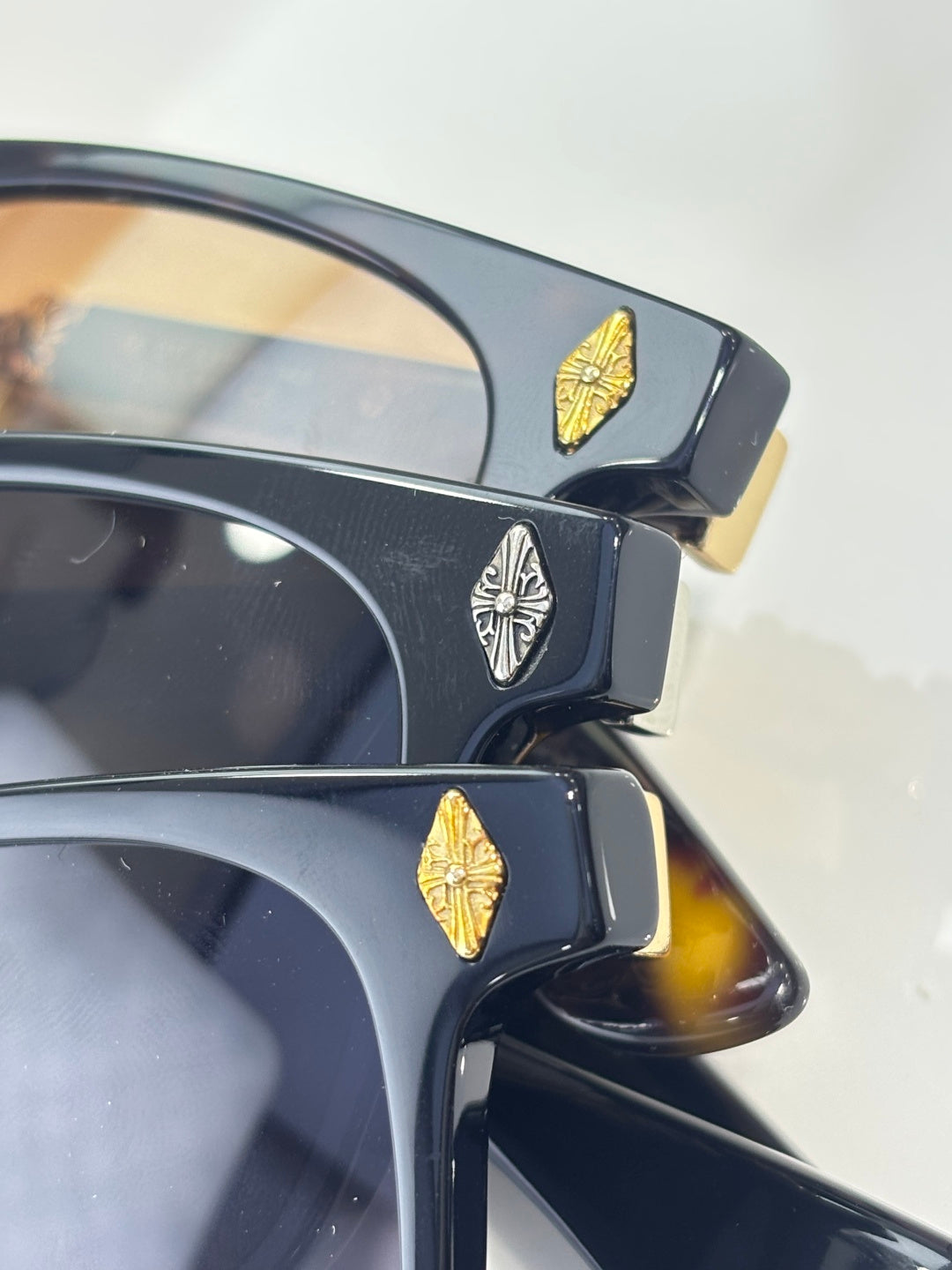 Sunglasses close-up with dark frames and gold butterfly-like emblem on temples.