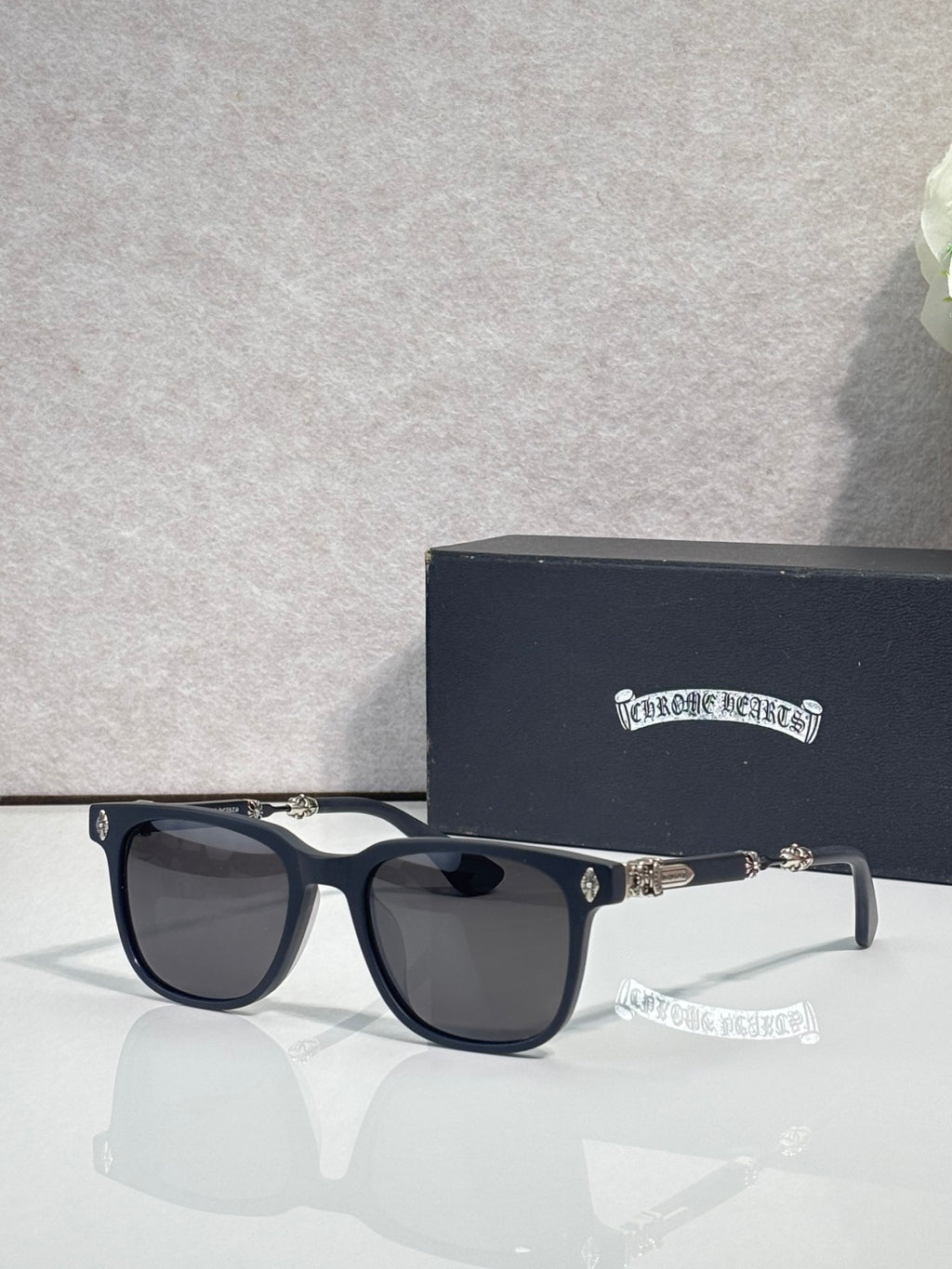 Sunglasses with dark frames and black lenses, gold-toned logo on temple.
