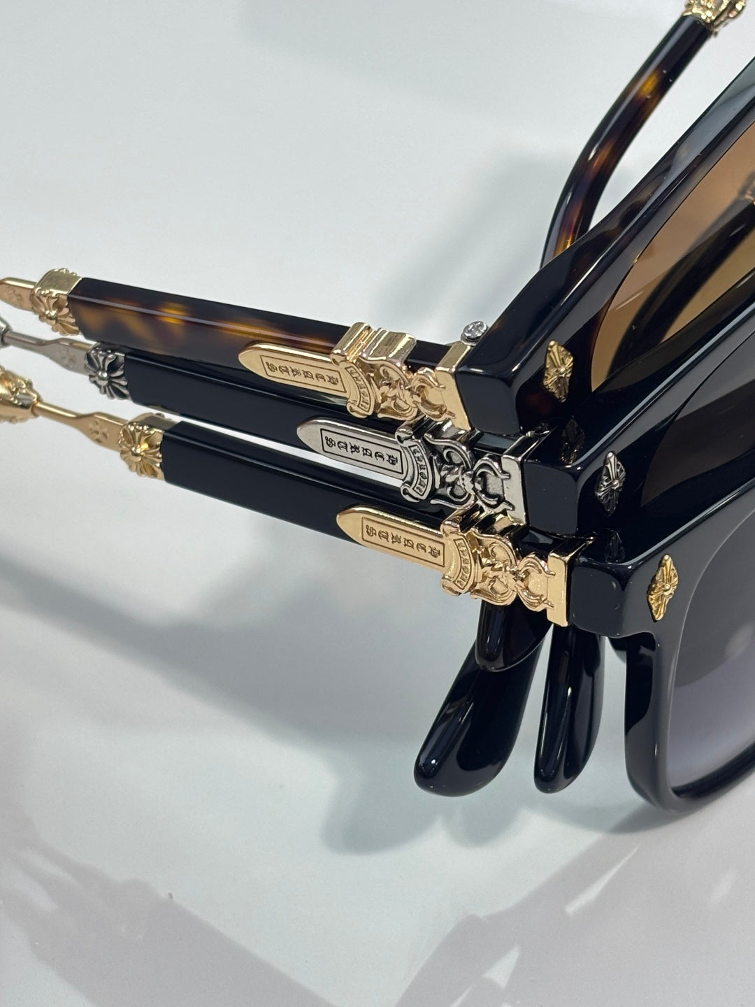 Sunglasses close-up: dark tortoise-style frame with gold ornate temple hardware.