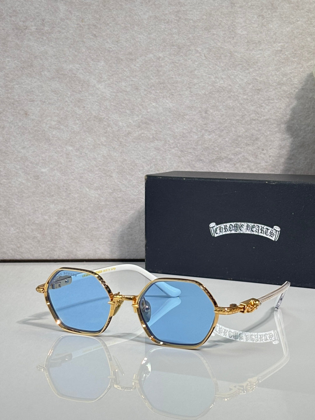 Round sunglasses with gold frames and blue-tinted lenses, clear bridge and ornate temples