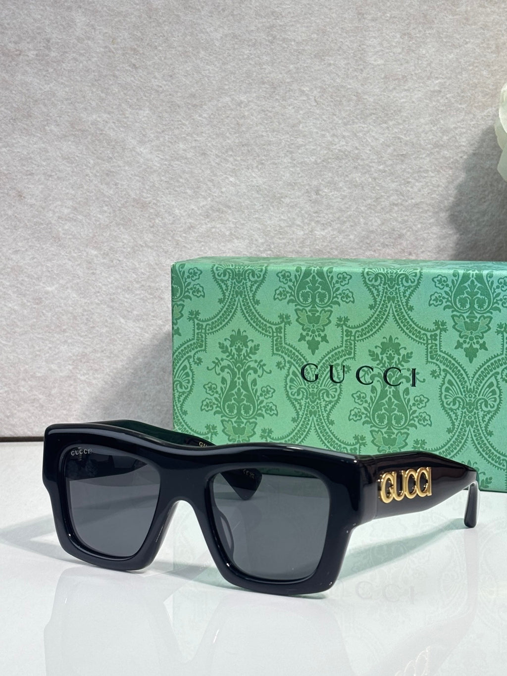 Gucci sunglasses with dark navy square frames and dark lenses, gold Gucci logo on temple