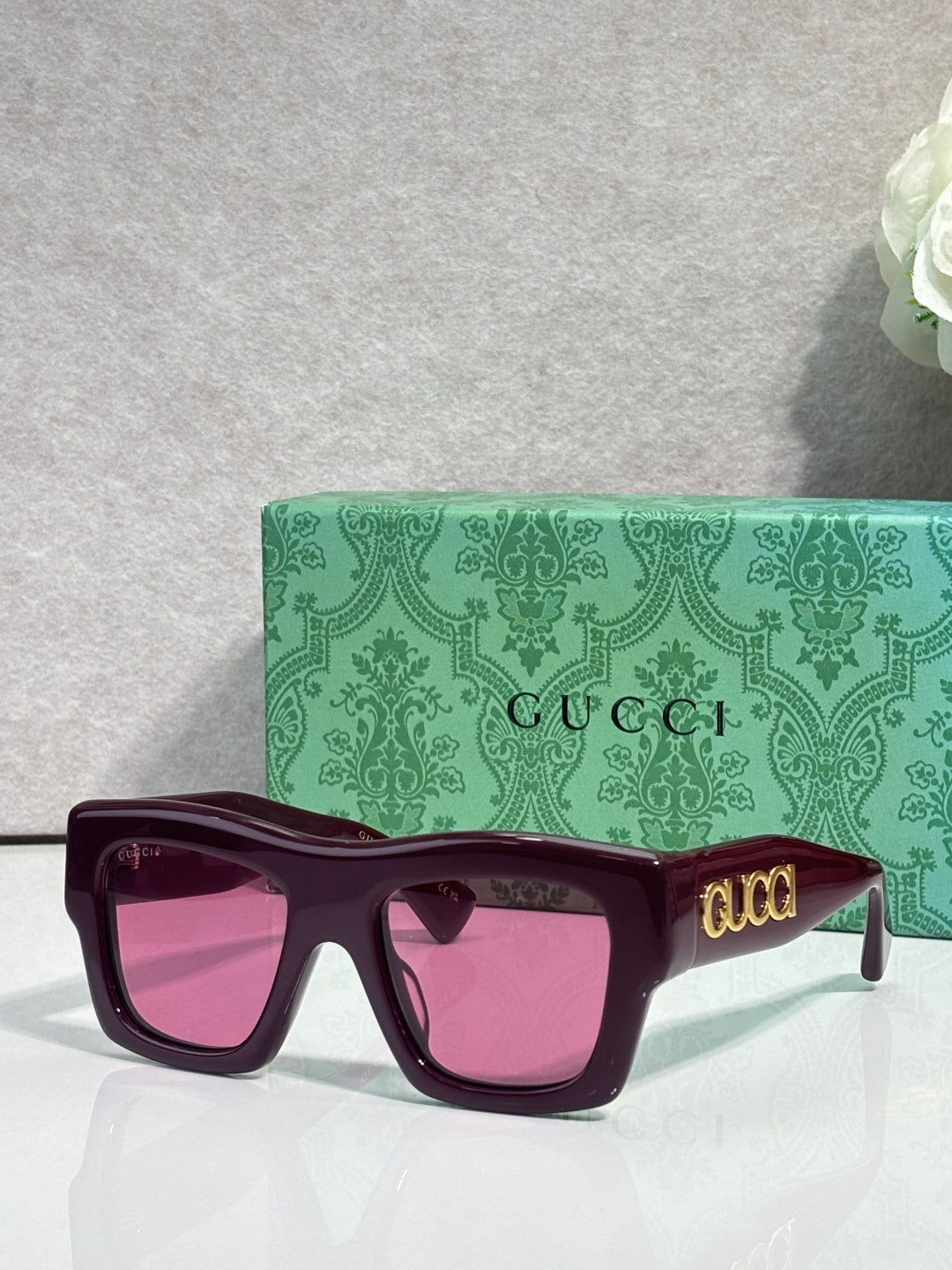Gucci sunglasses with deep purple square frames and pink lenses, gold Gucci logo on temple