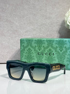Gucci sunglasses with dark teal square frames and light lenses, gold Gucci logo on temple
