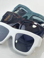 Gucci sunglasses with dark navy frames and dark lenses, white frame style below with gold logo