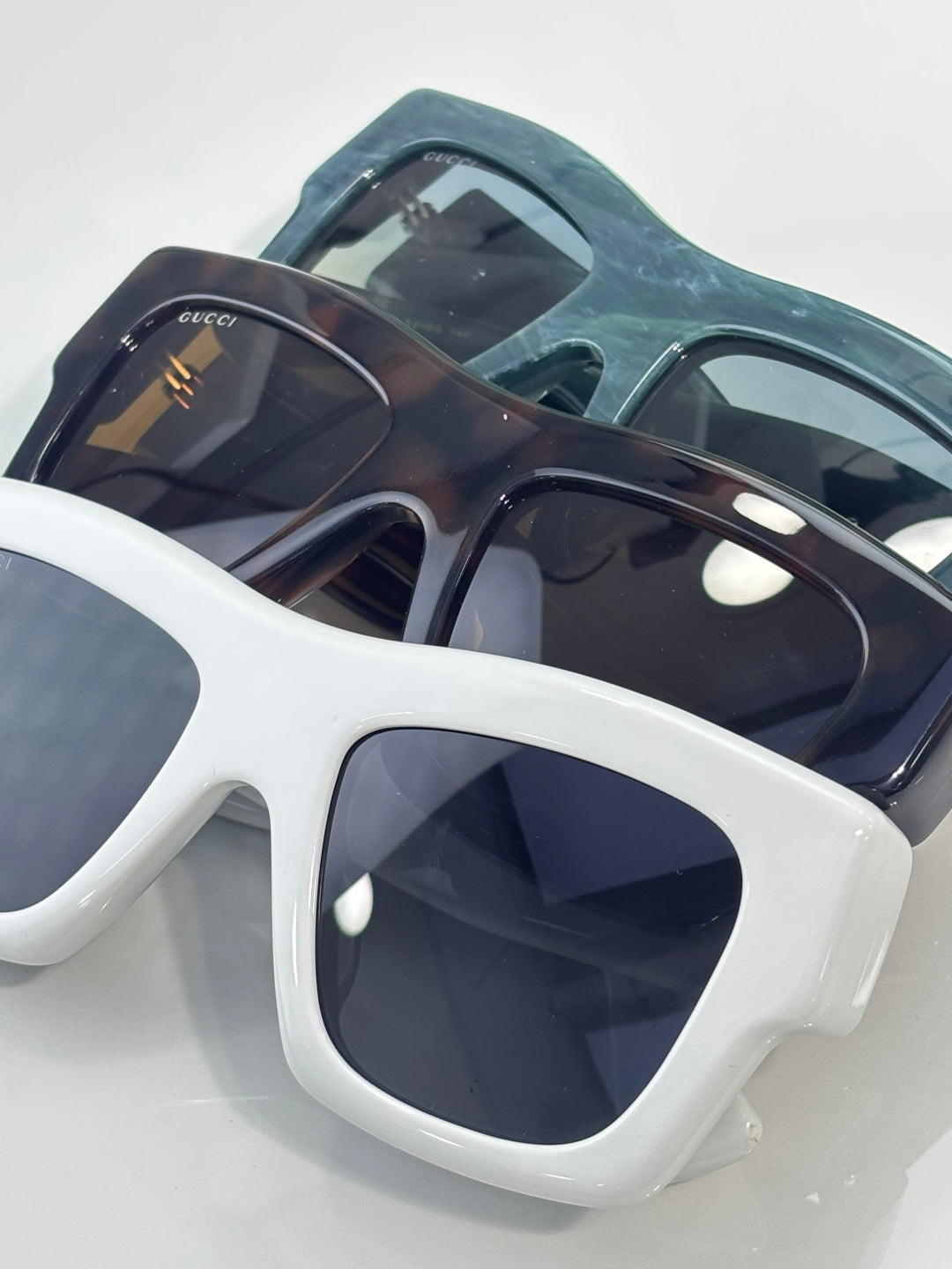 Gucci sunglasses with dark navy frames and dark lenses, white frame style below with gold logo