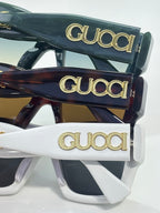 Gucci sunglasses stacked in dark green, tortoiseshell, and white frames with gold Gucci logos