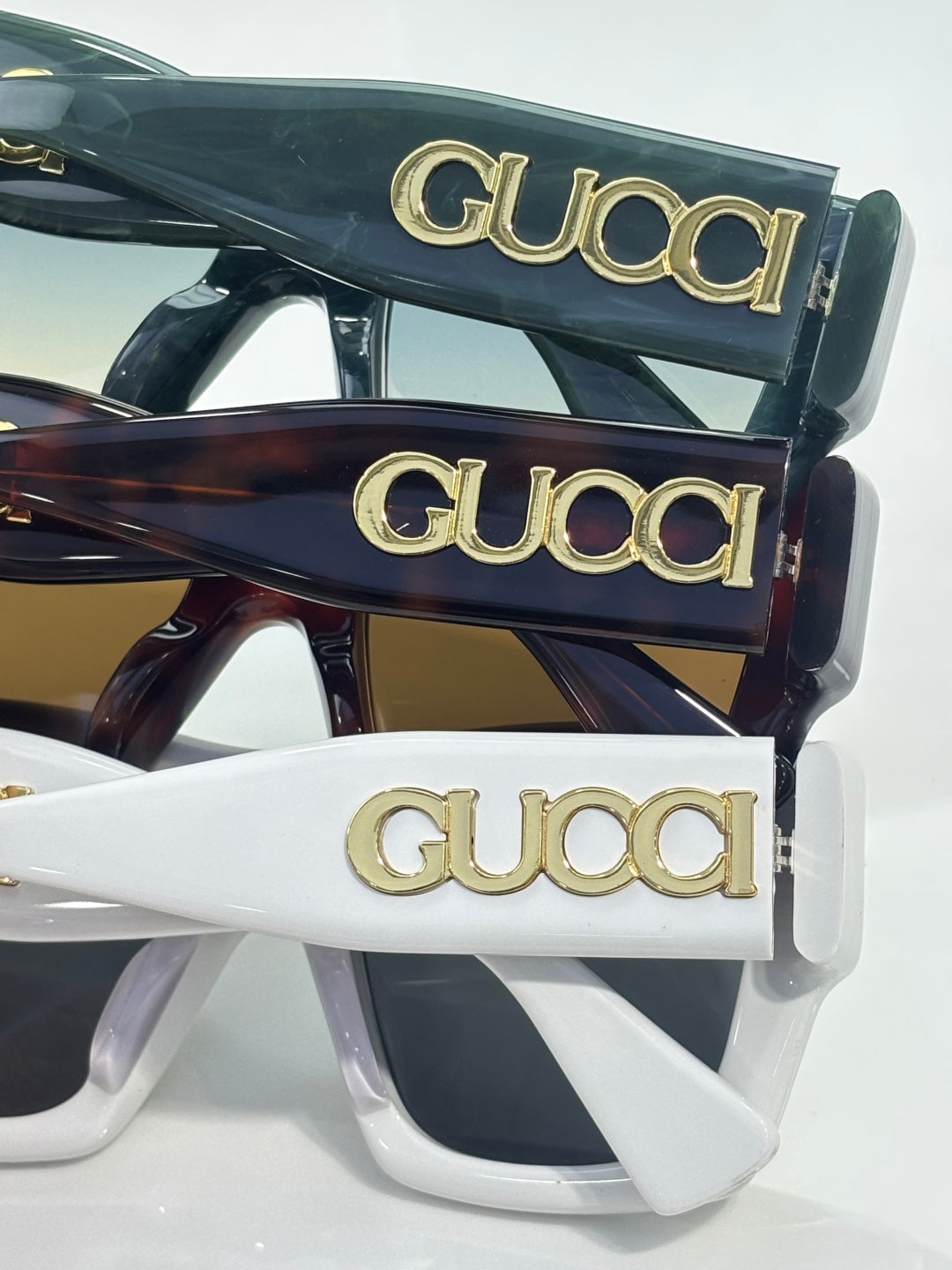 Gucci sunglasses stacked in dark green, tortoiseshell, and white frames with gold Gucci logos