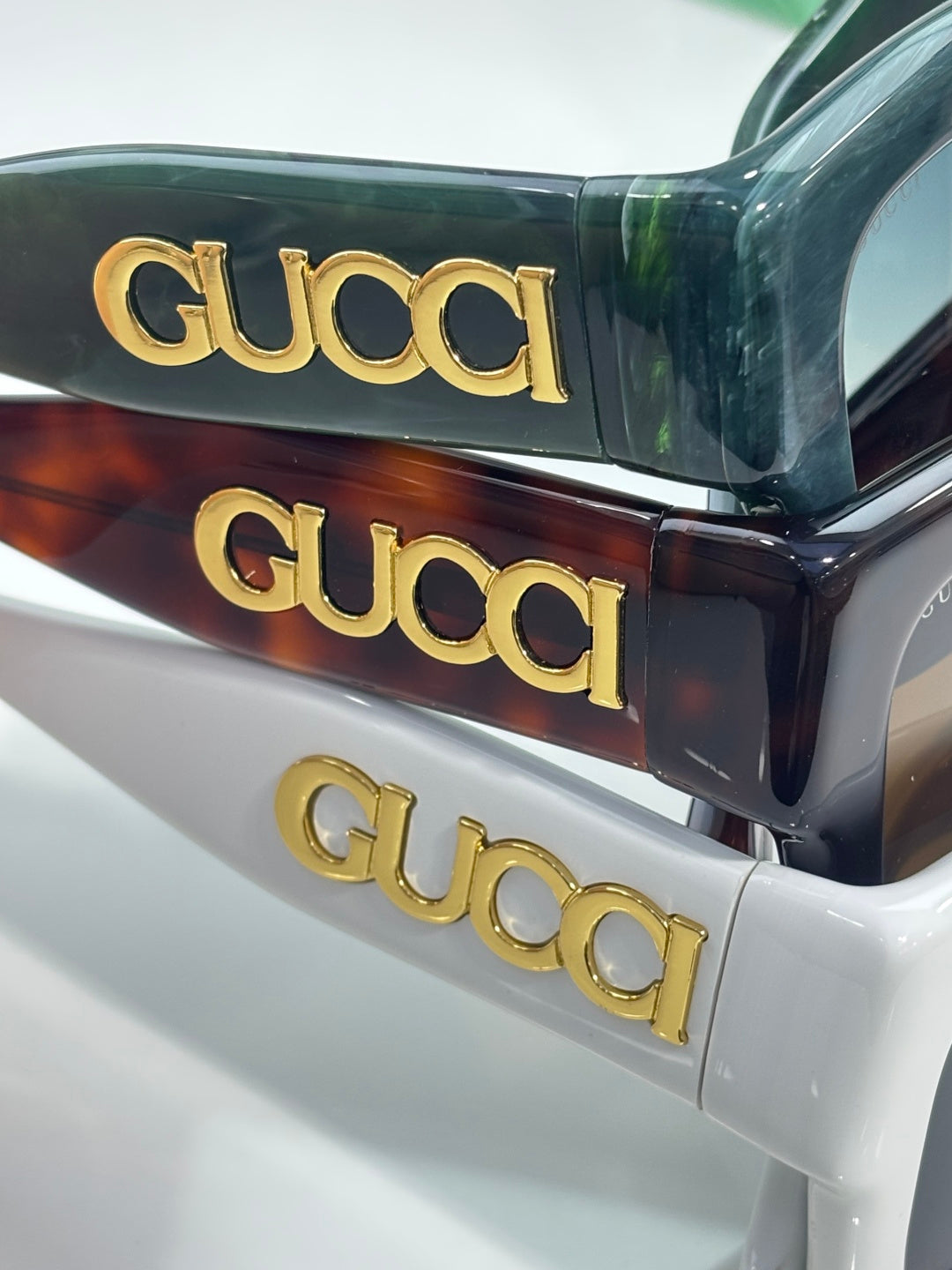 Gucci sunglasses showing stacked frames: dark green, tortoiseshell, and white with gold Gucci logos