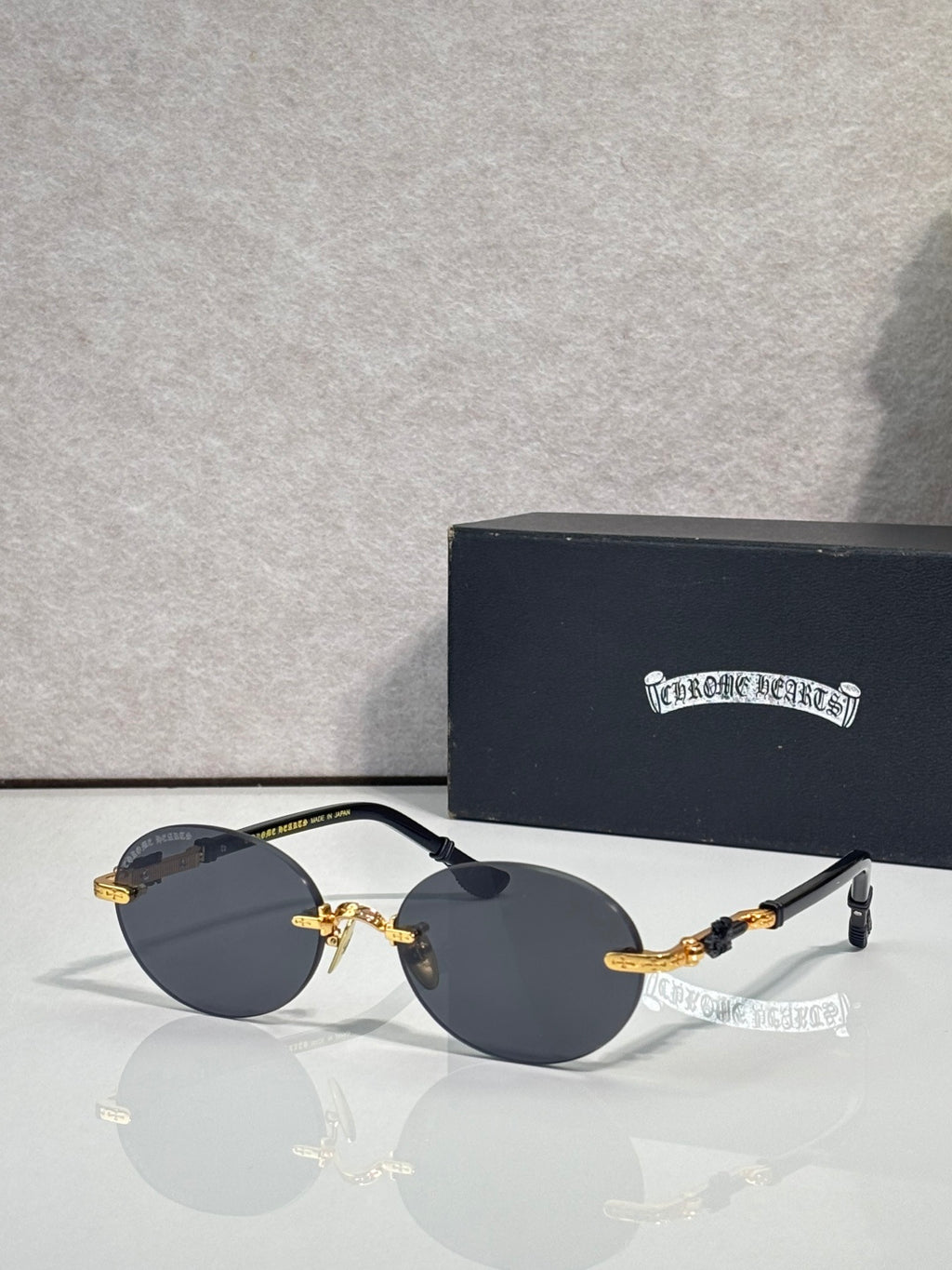 Round eyeglasses with dark lenses and gold accents on metal arms, with case