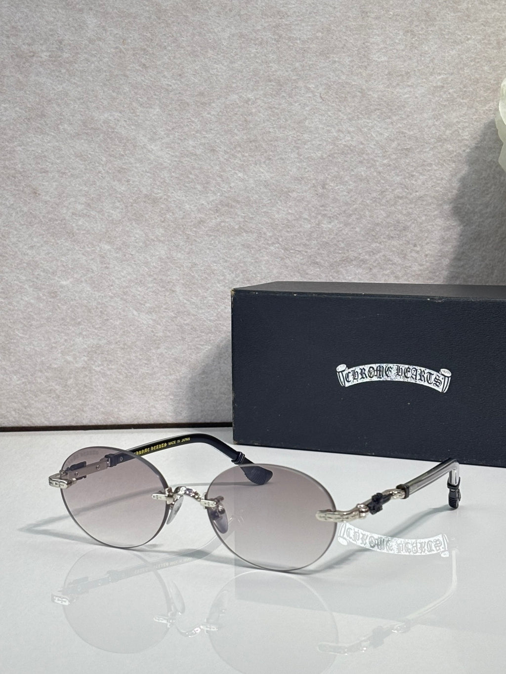 Round eyeglasses with silver-tone frame and dark lenses, shown with case behind
