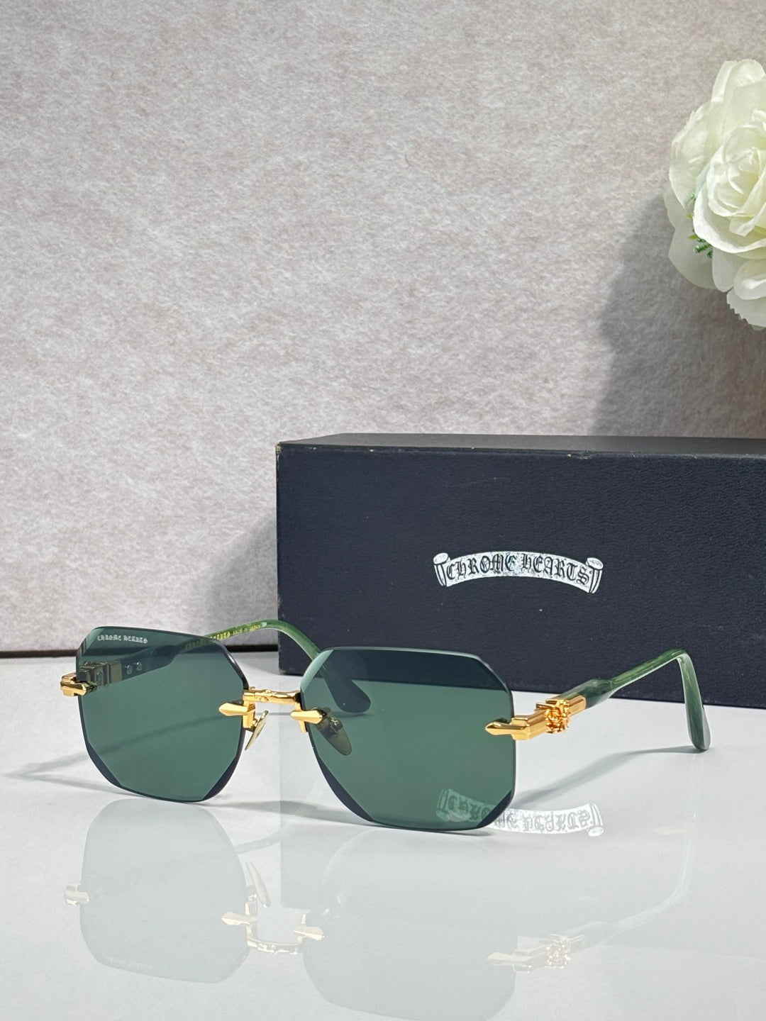 Chrome glasses with green-tinted lenses, black frame, gold-tone arms with logo