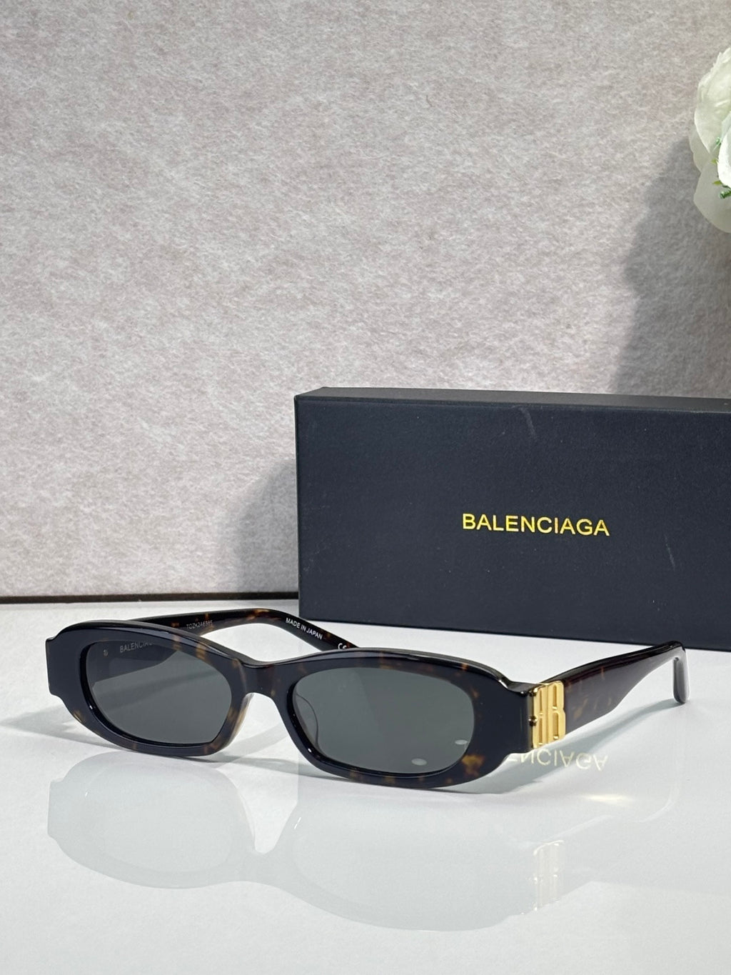 Balenciaga sunglasses with black frames and dark lenses, gold logo detail on temples