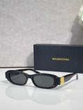 Balenciaga sunglasses with black frames and dark lenses, gold logo detail on temples