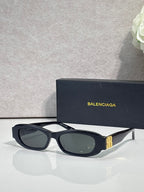Balenciaga sunglasses with black oval frames and dark lenses, gold logo on side hardware