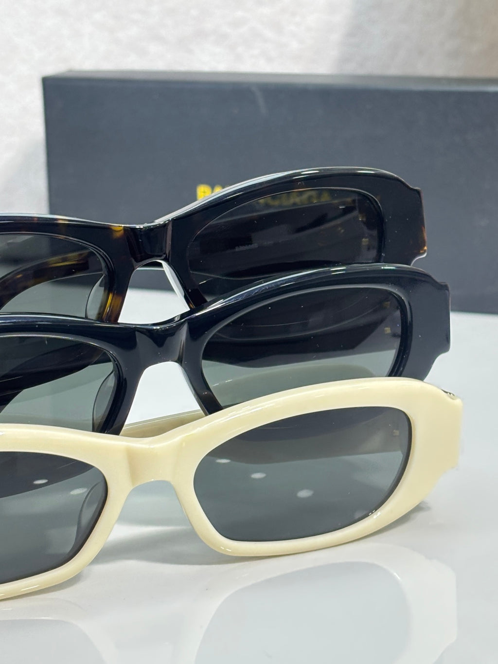 Balenciaga sunglasses pair: black and cream frames with dark lenses and gold logo hardware