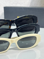 Balenciaga sunglasses pair: black and cream frames with dark lenses and gold logo hardware