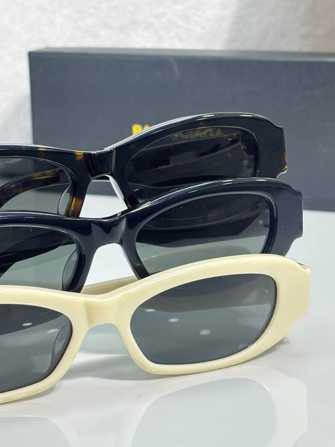 Balenciaga sunglasses pair: black and cream frames with dark lenses and gold logo hardware