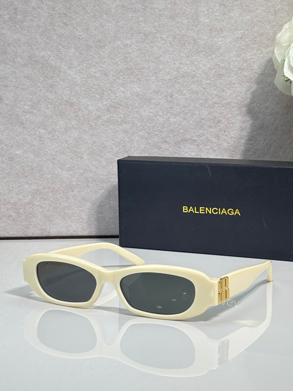 Balenciaga sunglasses with cream frames and dark lenses, gold logo accents on temples